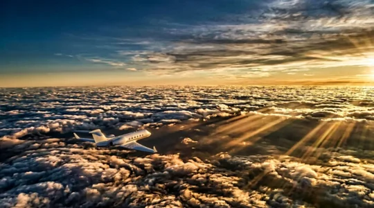 Vue aérienne d'un jet privé médical volant au-dessus des nuages dorés au coucher du soleil, symbolisant l'urgence du transport d'organes vitaux